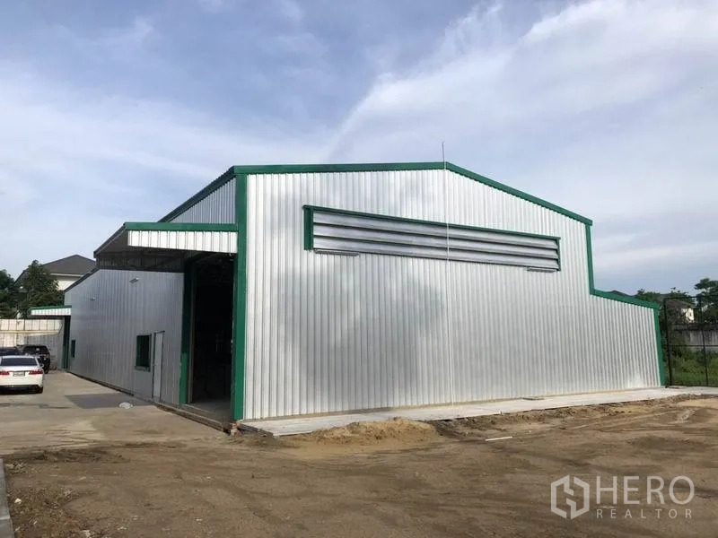 Warehouse for rent in Nonthaburi - Modern metal-clad warehouse exterior with green trim, wide driveway and loading yard under a clear sky.