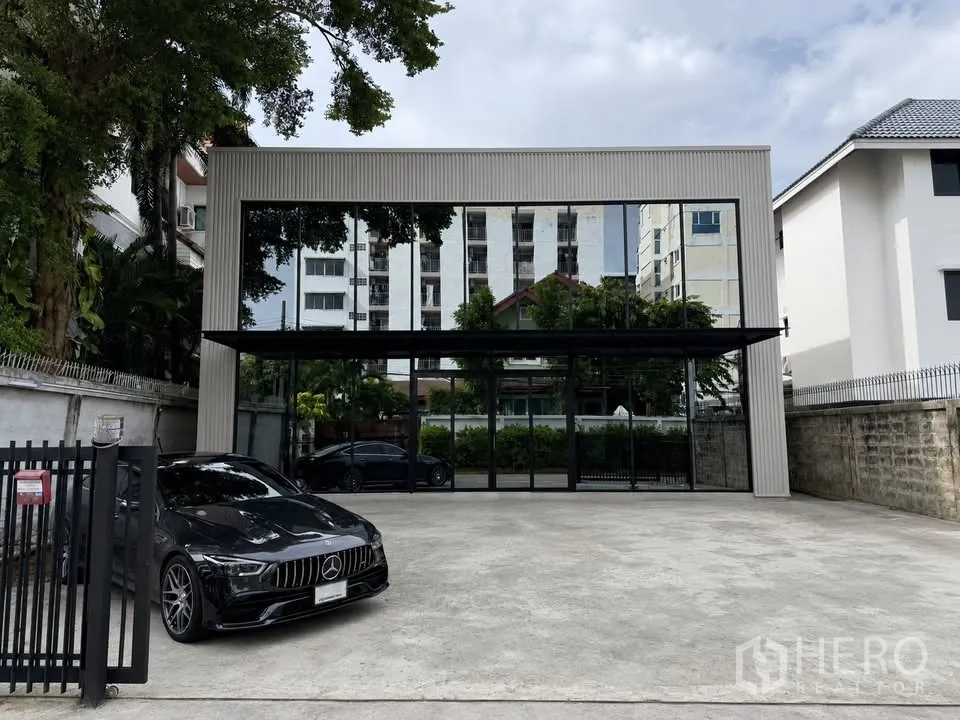 Warehouse for rent in Bang Na, Bangkok - Gated frontage with parking area and a modern glass facade building.