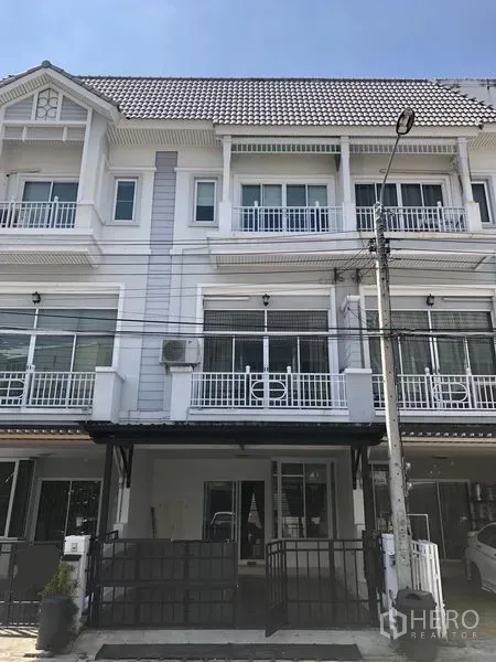 联排别墅 出租在Prawet, Bangkok - 三层联排别墅外观，白色立面，阳台与带门庭院车位。