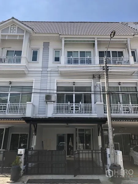 联排别墅 出租在Prawet, Bangkok - 三层联排别墅外观，白色立面，阳台与带门庭院车位。