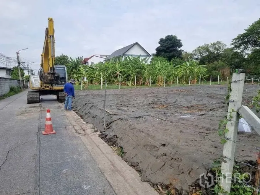Land for sale in Bang Khen, Bangkok - Filled and leveled land plot beside a quiet paved lane with an excavator and banana trees in Bang Khen, Bangkok.