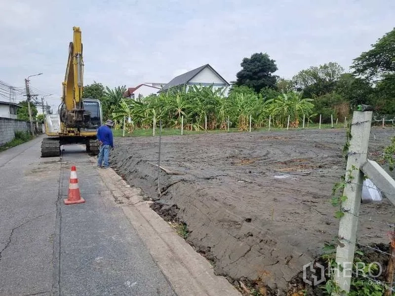 Land for sale in Bang Khen, Bangkok - Filled and leveled land plot beside a quiet paved lane with an excavator and banana trees in Bang Khen, Bangkok.