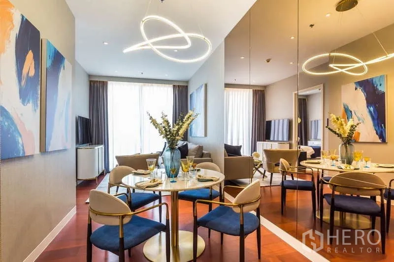 公寓 出租在Watthana, Bangkok - 餐区设圆桌、蓝色软包椅、镜面特色墙和雕塑感吊灯。