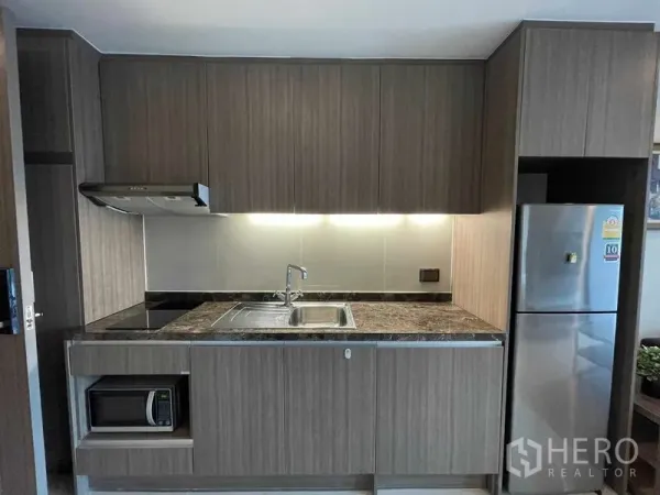 公寓 出租在Watthana, Bangkok - 现代厨房配大理石质感台面、感应炉、抽油烟机、水槽、微波炉与不锈钢冰箱。