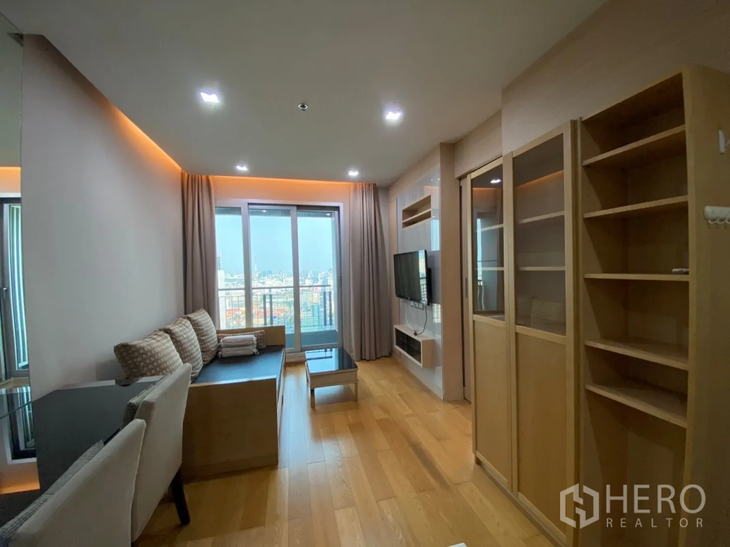 Condominium for rent in Ratchathewi, Bangkok - Cozy living room with sofa, wall-mounted TV, floor-to-ceiling windows and balcony city view.