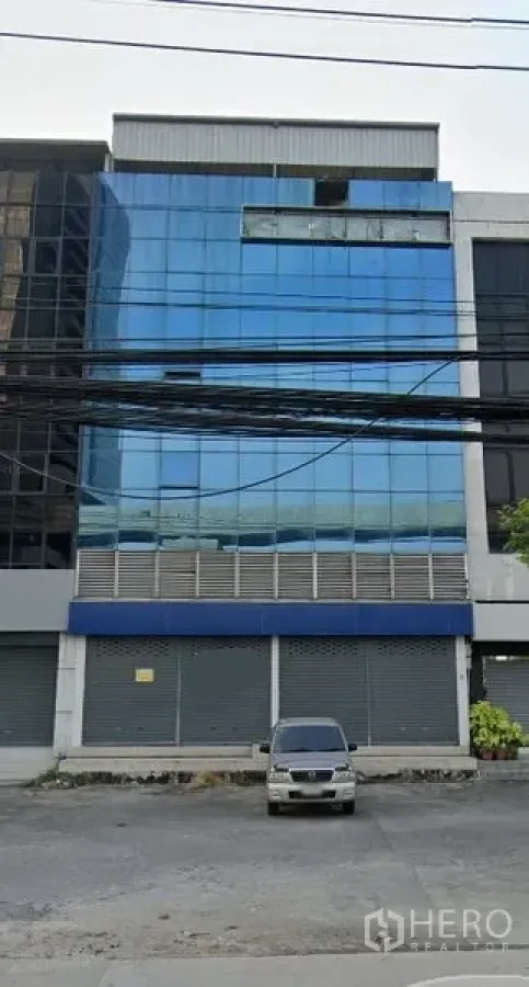 店屋 出租在Suan Luang, Bangkok - 多层蓝色玻璃幕墙的店屋，一层卷闸门，门前有停车位，位于城市街道。