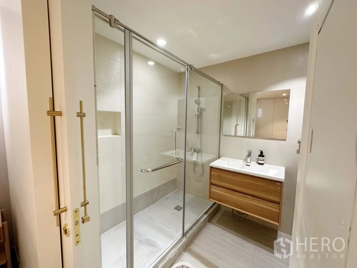 Condominium for rent or sale in Watthana, Bangkok - Modern bathroom with glass-enclosed shower and floating wooden vanity.