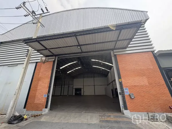 คลังสินค้า ให้เช่าในBang Phli, Samut Prakan - มุมมองด้านหน้าโกดังสูงโปร่ง พร้อมประตูทางเข้าขนาดใหญ่และผนังก่ออิฐสลับเมทัลชีท.