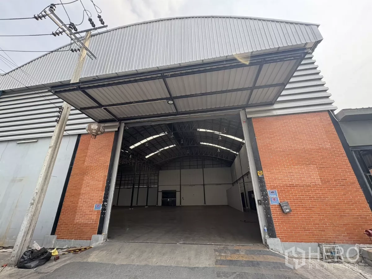 คลังสินค้า ให้เช่าในBang Phli, Samut Prakan - มุมมองด้านหน้าโกดังสูงโปร่ง พร้อมประตูทางเข้าขนาดใหญ่และผนังก่ออิฐสลับเมทัลชีท.