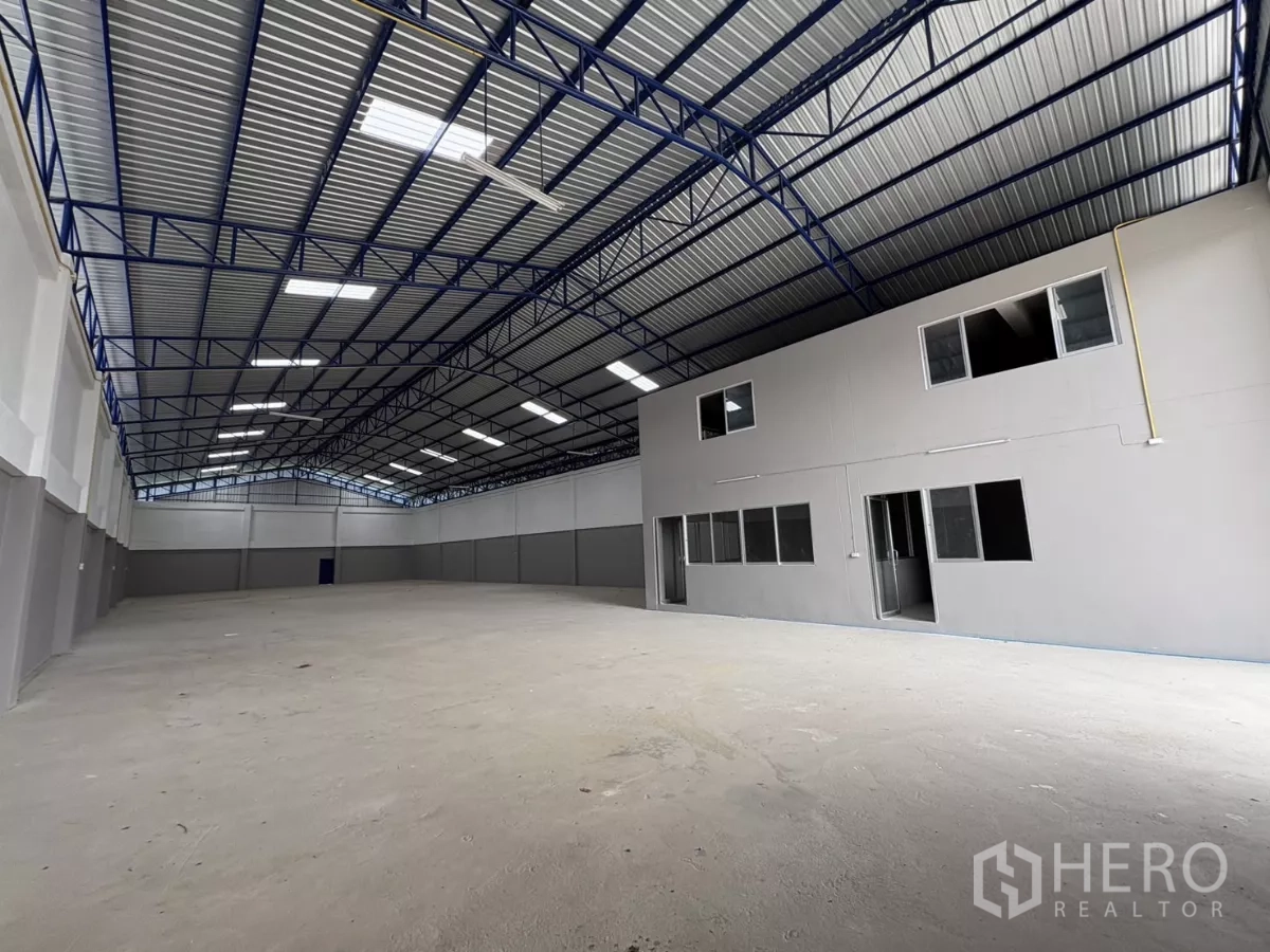 Warehouse for rent in Mueang Samut Prakan, Samut Prakan - Clear-span warehouse interior with steel truss roof and an attached two-storey office block.