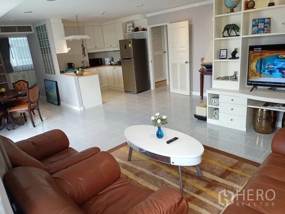 公寓 for rent in Watthana, Bangkok - 客厅配皮质沙发、椭圆茶几与内置电视柜，连接开放式厨房。
