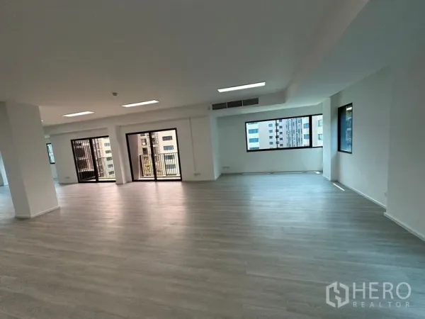 Office Space for rent - Open-plan office with light wood flooring, LED ceiling panels, large windows and sliding glass doors to small balconies in Sathon, Bangkok.
