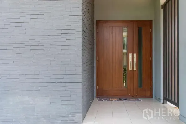 独立式住宅 出租或出售在Kanchanaburi - 入户处的实木大门，旁有灰色石材装饰墙。