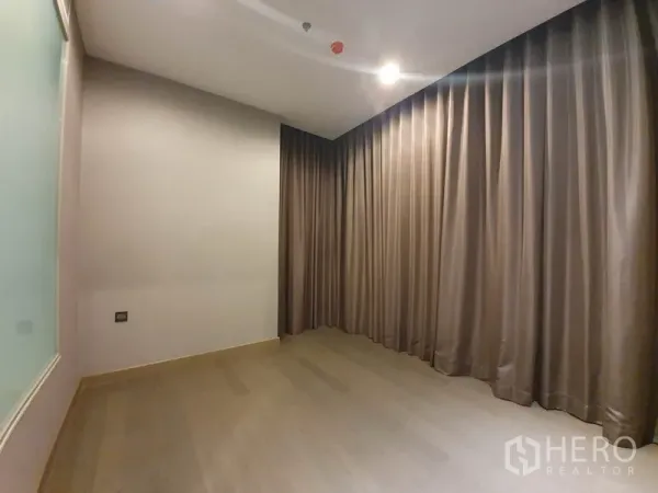 Condominium for rent in Huai Khwang, Bangkok - Empty bedroom or study with wood floors, floor-to-ceiling curtains, and soft lighting.