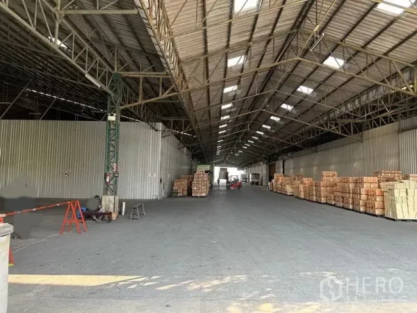 Warehouse for rent in Mueang Pathum Thani, Pathum Thani - Covered loading area inside a warehouse with stacked cartons and a wide driveway for forklifts and trucks.