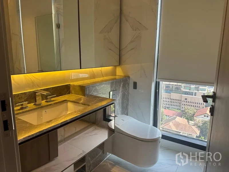 Condominium for rent - Luxury bathroom with stone vanity, backlit mirror and smart toilet beside a window.