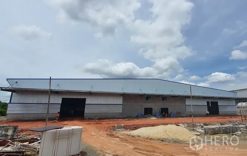 คลังสินค้า ให้เช่าในMueang Samut Sakhon, Samut Sakhon - ด้านหน้าโกดังยาว มีช่องประตูม้วนหลายจุดและวัสดุก่อสร้างวางอยู่