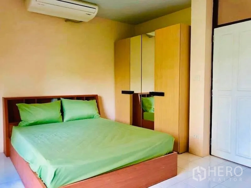 Townhouse for rent in Watthana, Bangkok - Cozy bedroom with green bedding, wardrobe and wall-mounted air conditioner.