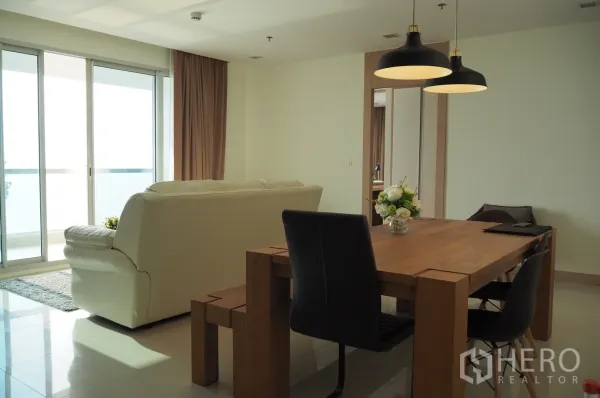 Condominium for rent in Bang Lamung, Chon Buri - Bright living and dining space with sliding doors to a sea-view balcony, wooden table and pendant lights.