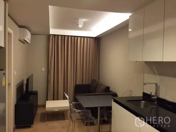 คอนโด ให้เช่าในWatthana, Bangkok - มุมนั่งเล่นมีโซฟา ทีวี โต๊ะทานอาหาร และไฟซ่อนฝ้า ถัดจากตู้ครัวสีขาวเงา