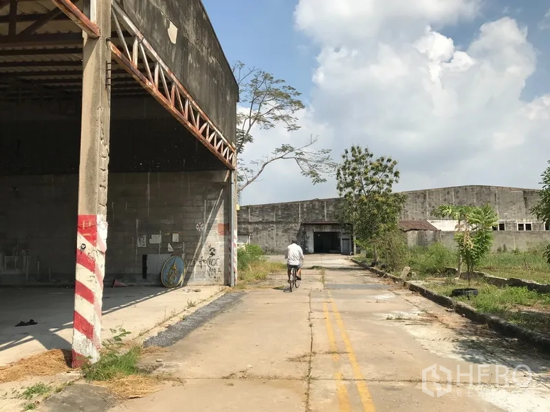 Land for rent in Phra Pradaeng, Samut Prakan - Exterior service lane beside old warehouse buildings with greenery along the edge.