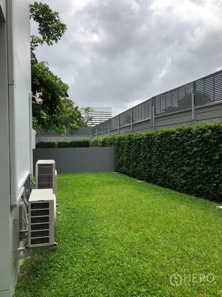 บ้าน ให้เช่าในWatthana, Bangkok - สวนข้างบ้านส่วนตัว สนามหญ้าเขียว รั้วพุ่มไม้สูง และรั้วบังสายตา ข้างคอมเพรสเซอร์แอร์