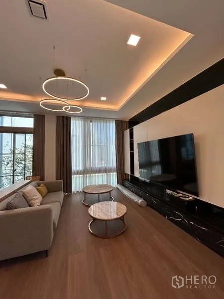 Detached House for rent in Saphan Sung, Bangkok - Living room with sofa, large TV wall and circular ceiling lights.