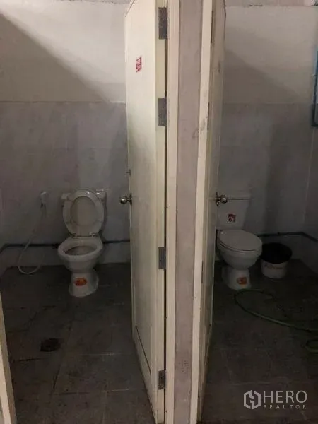 Warehouse for rent in Pak Kret, Nonthaburi - Separate tiled restroom stalls inside the warehouse with flush toilets and hand sprayers.