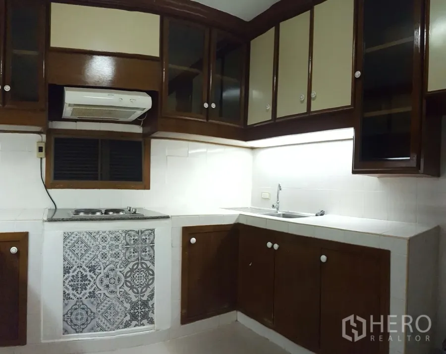 Condominium for rent or sale in Watthana, Bangkok - U-shaped kitchen with wood cabinetry, tiled backsplash, cooktop and sink in a Bangkok condo.