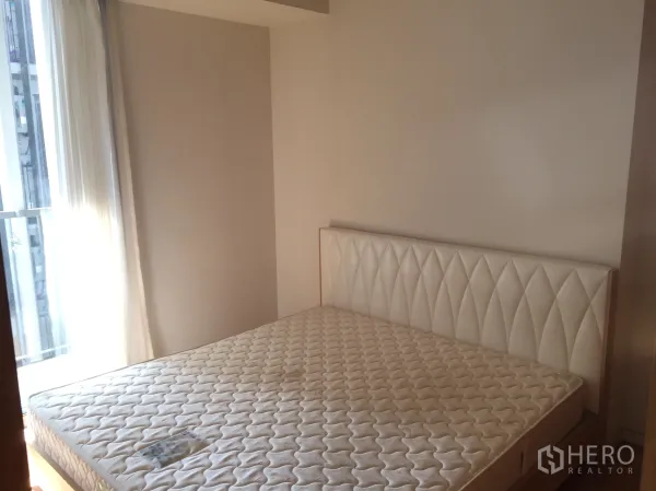 Condominium for sale in Sathon, Bangkok - Bright bedroom with upholstered headboard and large window letting in city light.