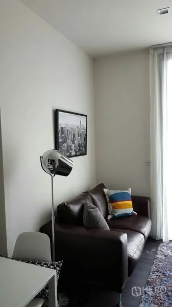Condominium for rent in Watthana, Bangkok - Cozy sofa corner beneath a cityscape artwork beside a tall window and textured rug.