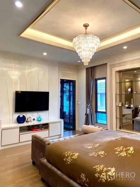 Detached House for rent or sale in Prawet, Bangkok - Master bedroom with chandelier, media console, and access to a balcony.