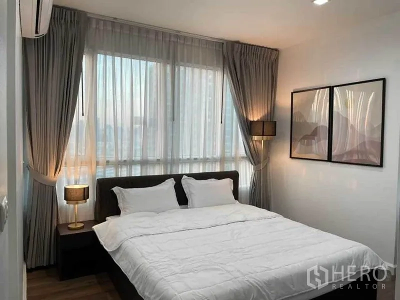 Condominium for rent or sale in Watthana, Bangkok - Master bedroom with large corner windows, bedside lamps and soft drapes.