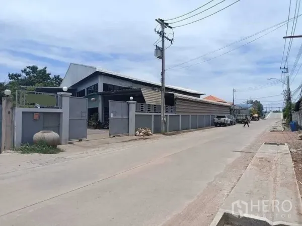 คลังสินค้า ขายในSamut Sakhon - มุมมองถนนหน้าโกดัง มีกำแพงรั้วสูง สายไฟฟ้า และถนนคอนกรีตกว้าง ในอำเภอเมืองสมุทรสาคร