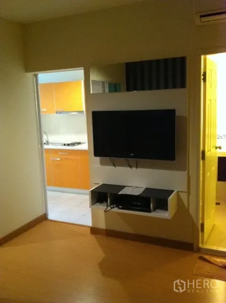 คอนโด ให้เช่าในWatthana, Bangkok - ชั้นวางทีวีติดผนังหันหน้าโซฟา ถัดไปเป็นทางเข้าครัวแยกตู้สีส้มสว่าง