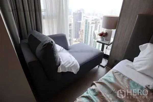 Condominium for rent in Watthana, Bangkok - Bedroom reading nook with chaise lounge by floor-to-ceiling window overlooking Bangkok skyline.