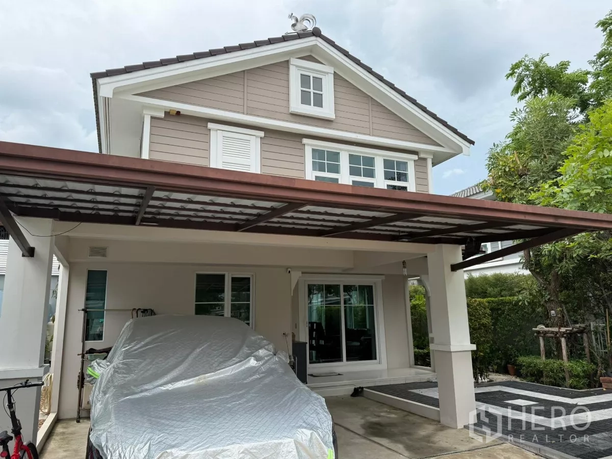 Townhouse for rent or sale in Sai Mai, Bangkok - Close view of the carport and front porch beneath a metal roof beside landscaped hedges.