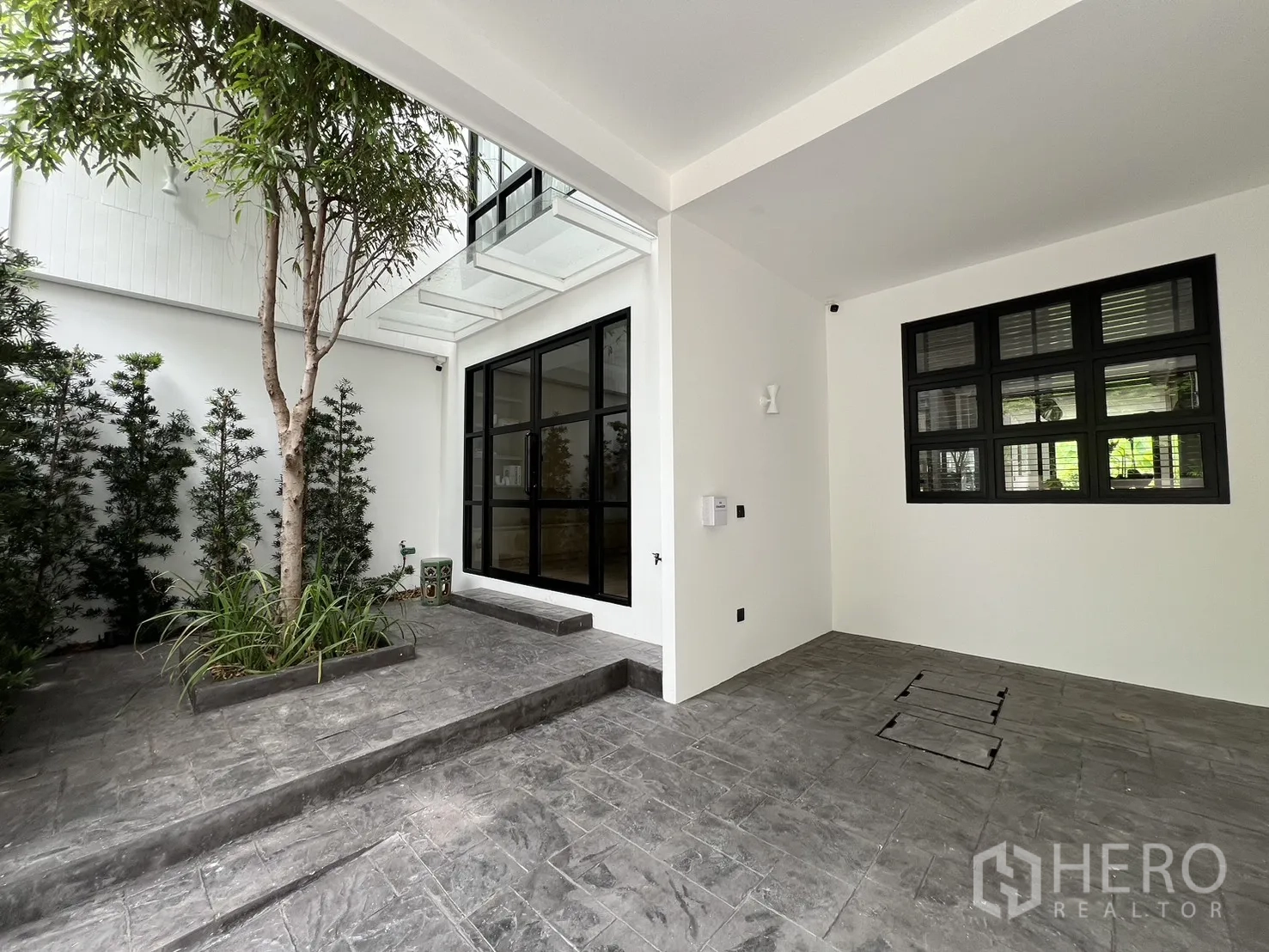 Townhouse for sale in Watthana, Bangkok - Covered carport opening onto a courtyard with steps and large black-framed windows.