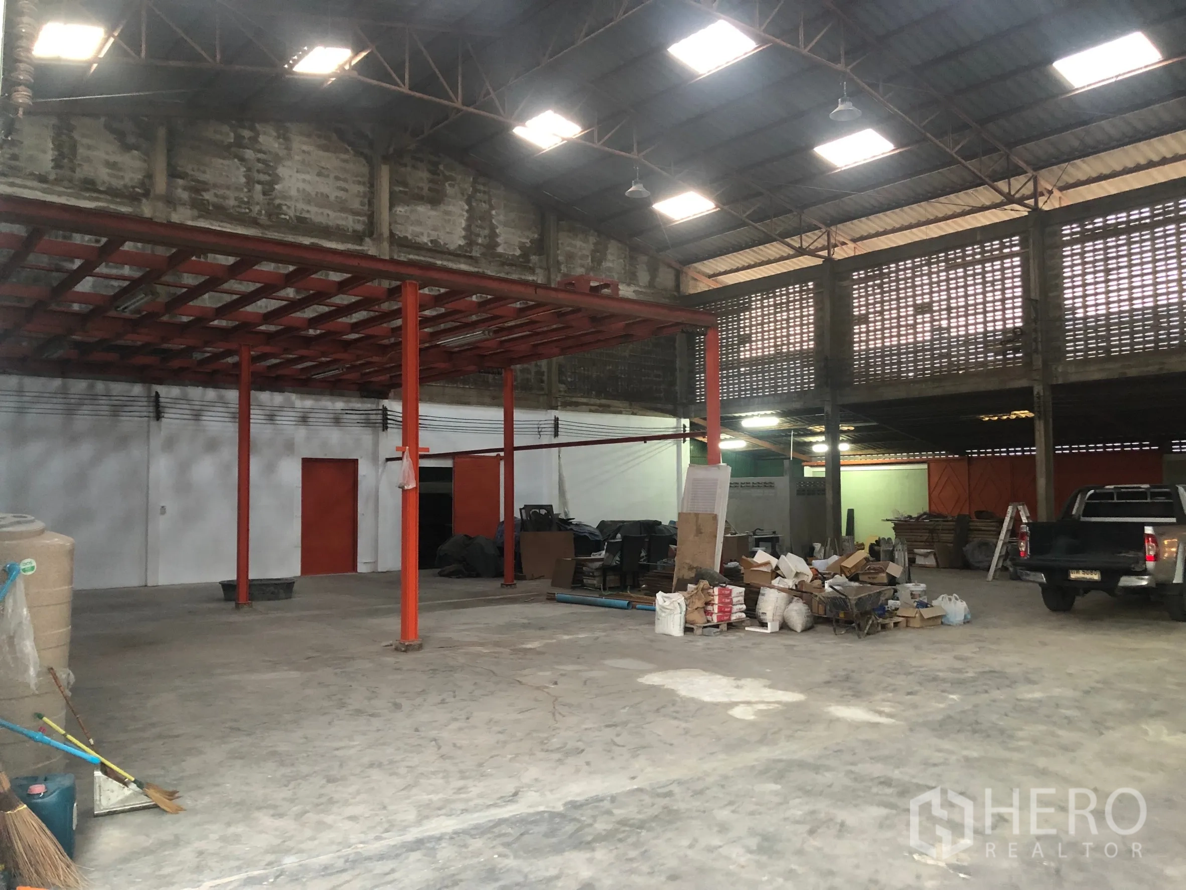 Warehouse for rent in Min Buri, Bangkok - Wide concrete-floored warehouse area with pickup trucks, skylights and stacked materials.