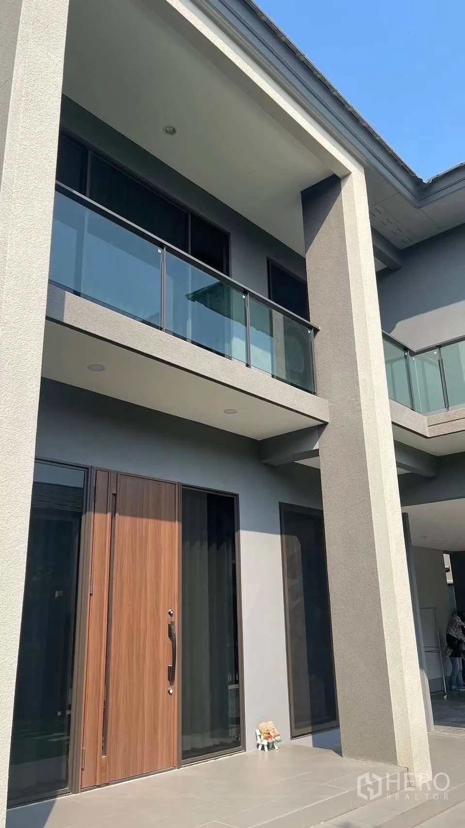 Detached House for rent in Prawet, Bangkok - Close view of the facade with glass balcony, columns and wooden front door.