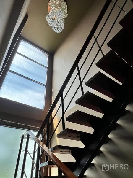 Detached House for sale in Prawet, Bangkok - Modern open staircase with metal railings next to a tall frosted window and chandelier.