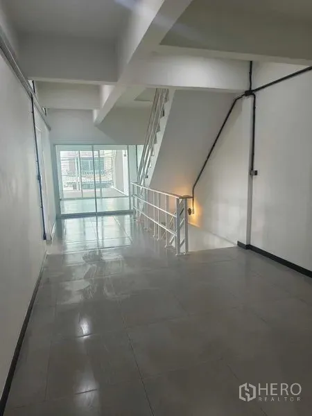 Townhouse for sale in Bang Phlat, Bangkok - Hallway with staircase and glossy tiles leading to a glass-enclosed balcony.