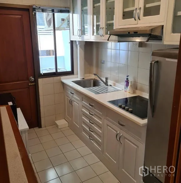 คอนโด ให้เช่าหรือขายในWatthana, Bangkok - ครัวแบบแกลลีย์ตู้สีขาว บานกระจก เตาไฟฟ้า อ่างล้างจาน และหน้าต่างระบายอากาศ