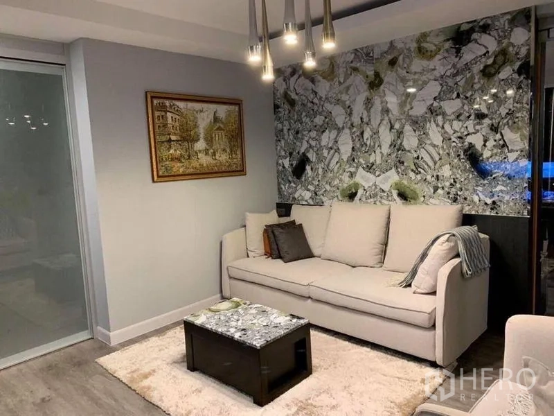 คอนโด ขายในKhlong Toei, Bangkok - ห้องนั่งเล่นคอนโดในคลองเตย โซฟาสีครีม ผนังลายหินอ่อน โคมไฟแขวน และประตูกระจกบานเลื่อน