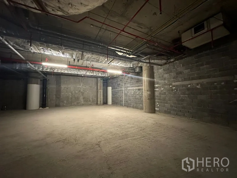 พื้นที่ขายปลีก ให้เช่า - ภายในร้านค้ายังไม่ตกแต่ง เพดานสูง ไฟเส้น สายสปริงเกลอร์สีแดง และเสาโครงสร้าง