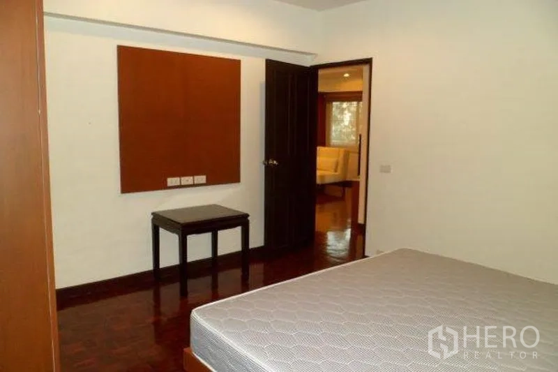 คอนโด ให้เช่าในPathum Wan, Bangkok - ห้องนอนเรียบง่าย พื้นไม้ เตียงวางฐาน พร้อมโต๊ะข้าง มองออกไปยังโซนรับแขก