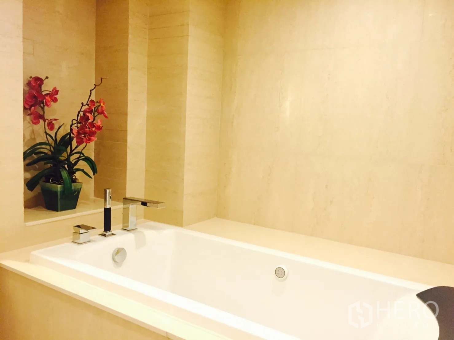 公寓 出租或出售在Sathon, Bangkok - 米色石材台面的深浸浴缸，配铬合金龙头与装饰兰花。