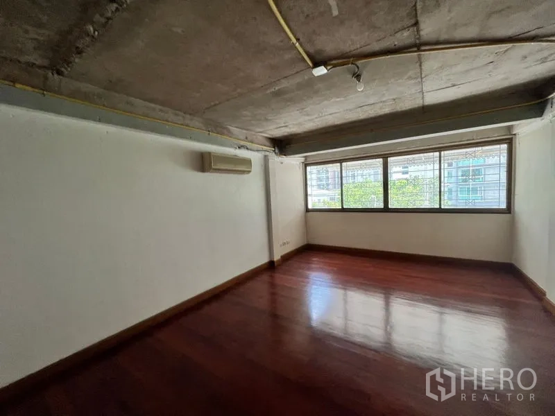Townhouse for rent in Khlong Toei, Bangkok - Upper-floor room with large windows, exposed ceiling and wood flooring.