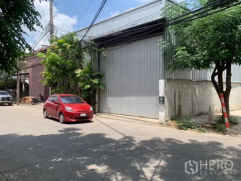 คลังสินค้า ให้เช่าในBang Kapi, Bangkok - มุมมองด้านหน้าโกดัง เห็นทางเข้า พื้นที่ริมถนน ต้นไม้ และกำแพงล้อมรอบ