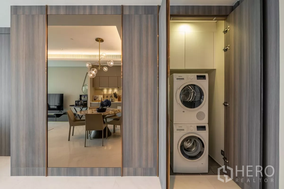 Condominium for rent or sale in Pathum Wan, Bangkok - Laundry closet with stacked washer and dryer hidden behind wood panels.